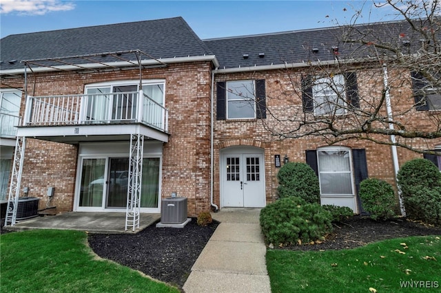 back of property featuring brick siding, roof with shingles, a balcony, and central air condition unit