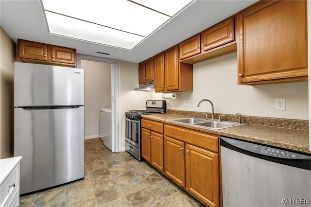 kitchen with appliances with stainless steel finishes, brown cabinets, washer / clothes dryer, under cabinet range hood, and a sink