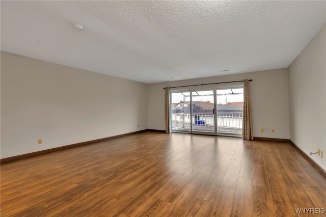 unfurnished room with a textured ceiling, wood finished floors, and baseboards