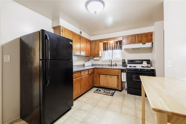 kitchen featuring brown cabinetry, freestanding refrigerator, a sink, gas range, and under cabinet range hood