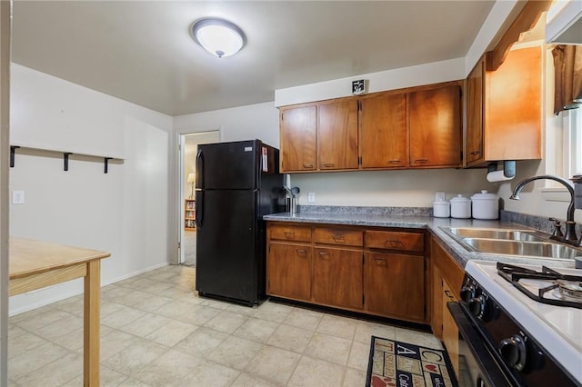 kitchen featuring brown cabinetry, freestanding refrigerator, a sink, and gas range oven