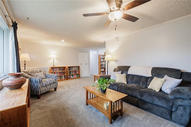 living area with a textured ceiling, carpet floors, ornamental molding, and a ceiling fan