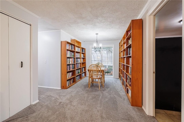 unfurnished room with wall of books, an inviting chandelier, crown molding, a textured ceiling, and carpet floors