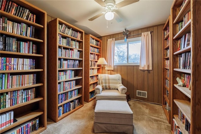 living area featuring wooden walls, visible vents, ceiling fan, and wall of books