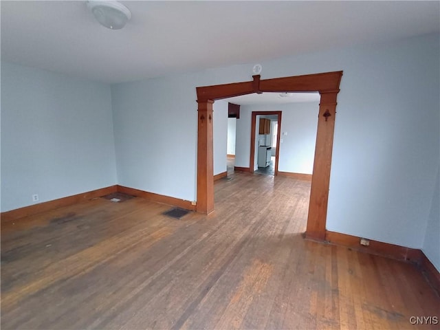 empty room with wood finished floors, visible vents, and baseboards