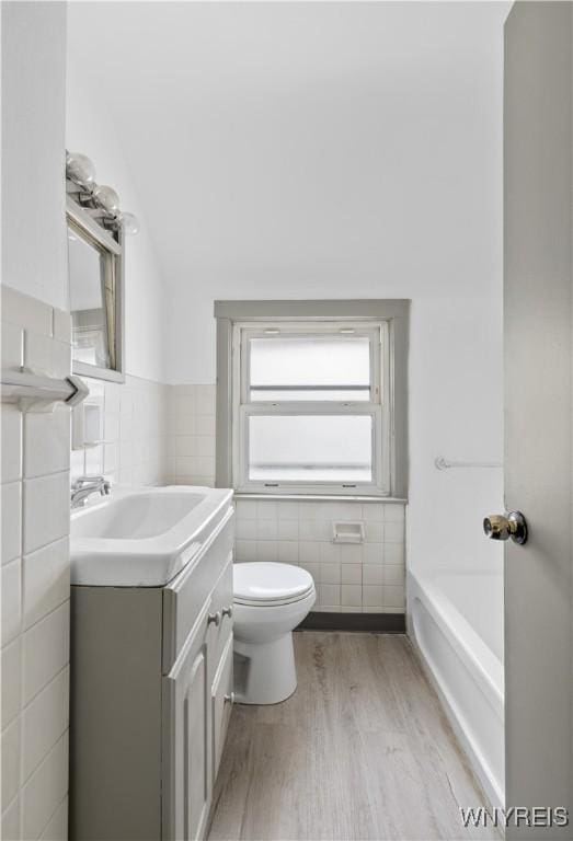 full bathroom featuring a washtub, tile walls, toilet, and vanity