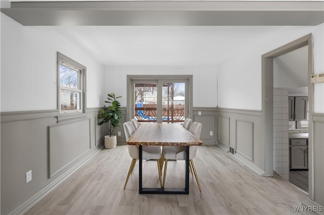 dining room with light wood-style floors, a decorative wall, a wealth of natural light, and wainscoting