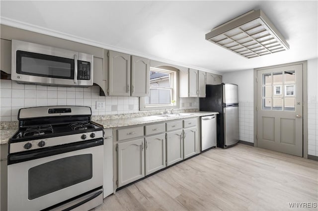 kitchen with gray cabinets, backsplash, appliances with stainless steel finishes, light wood-style floors, and a sink