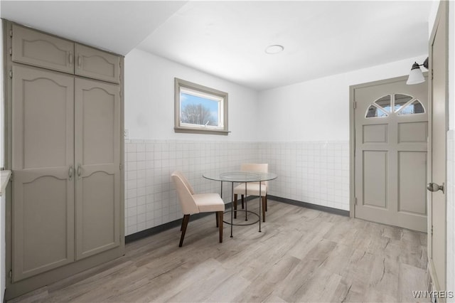 dining area featuring light wood finished floors, wainscoting, and tile walls