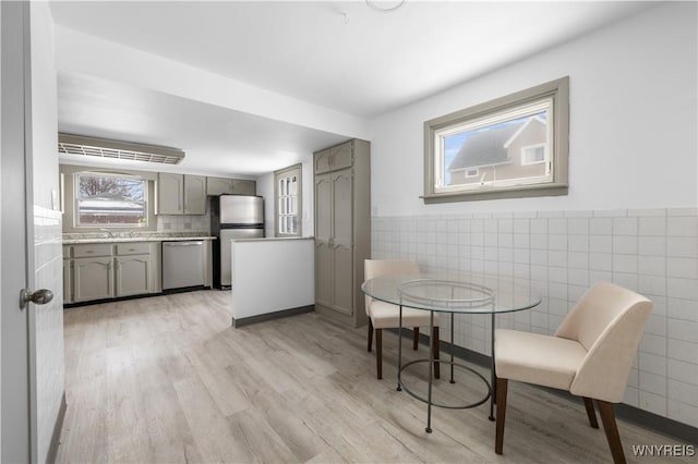 dining area featuring light wood-style floors, a wainscoted wall, and tile walls