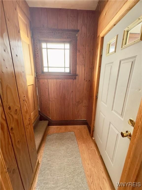 entryway featuring baseboards, wood walls, and light wood finished floors