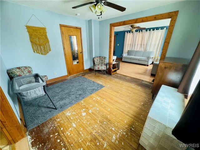 living area featuring ceiling fan, baseboards, and wood finished floors