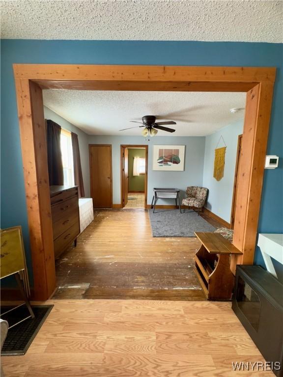 living room featuring ceiling fan, a textured ceiling, baseboards, and wood finished floors