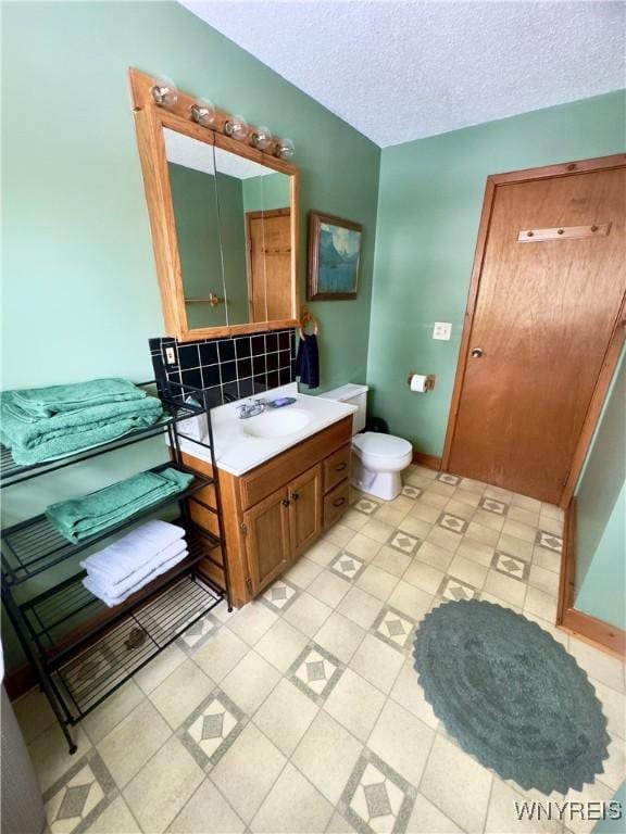 bathroom featuring a textured ceiling, vanity, toilet, and baseboards