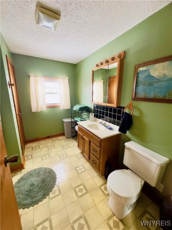 bathroom featuring a textured ceiling, toilet, vanity, baseboards, and tile patterned floors