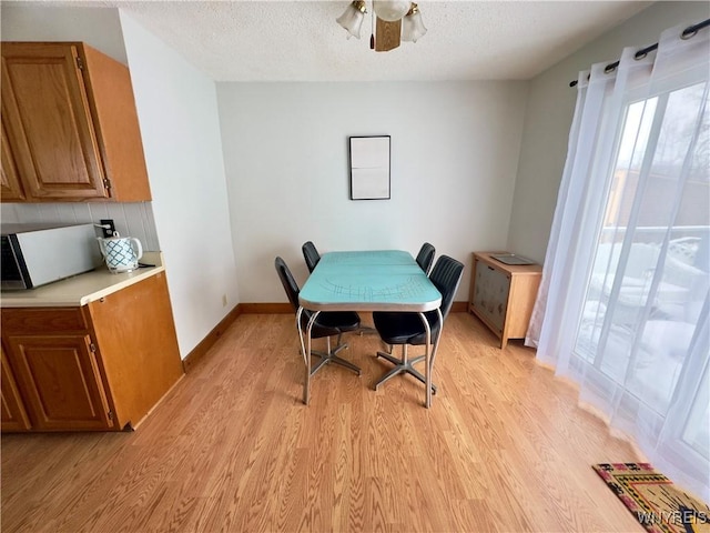 dining room featuring a ceiling fan, light wood-type flooring, a textured ceiling, and baseboards