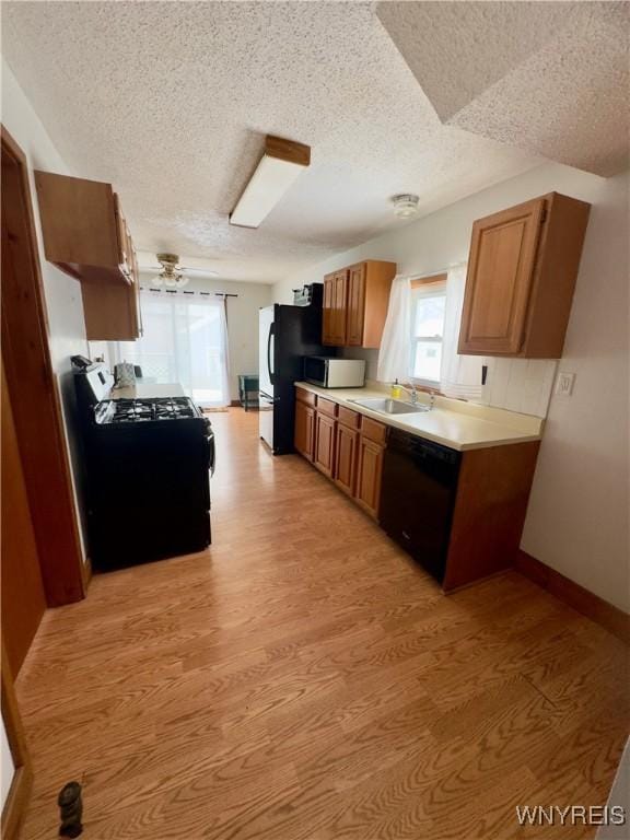 kitchen featuring a sink, light countertops, black appliances, light wood finished floors, and brown cabinetry