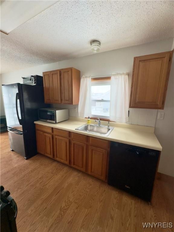 kitchen with a sink, black dishwasher, light wood-type flooring, freestanding refrigerator, and stainless steel microwave