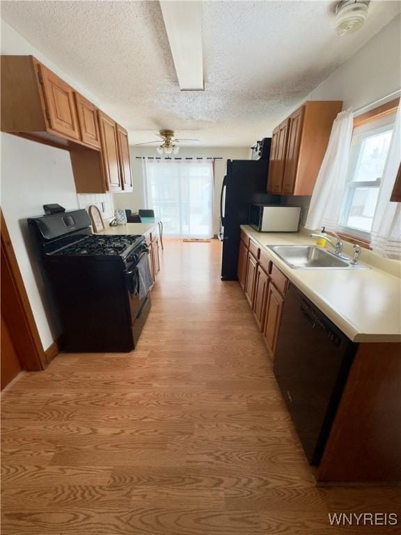 kitchen featuring black appliances, a sink, light countertops, and a healthy amount of sunlight