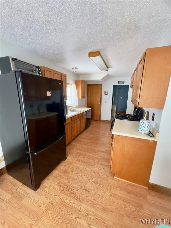 kitchen featuring dishwashing machine, freestanding refrigerator, light countertops, and light wood finished floors