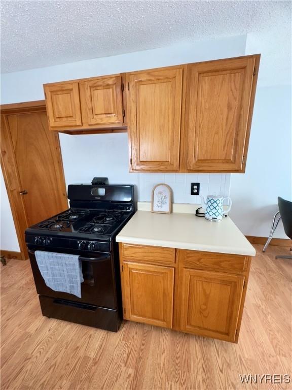 kitchen with a textured ceiling, light countertops, light wood-style floors, and black gas range oven