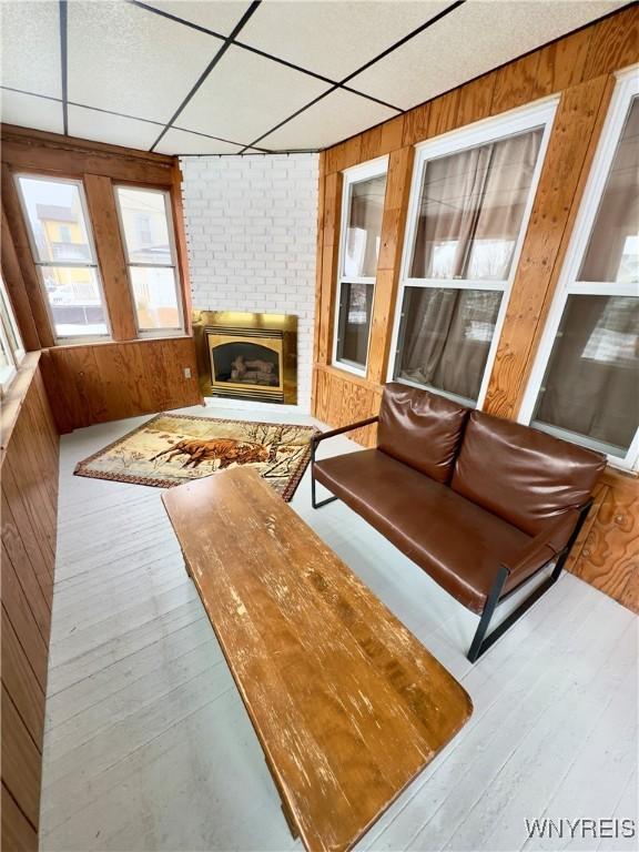 interior space with a drop ceiling, a brick fireplace, wood finished floors, and wooden walls