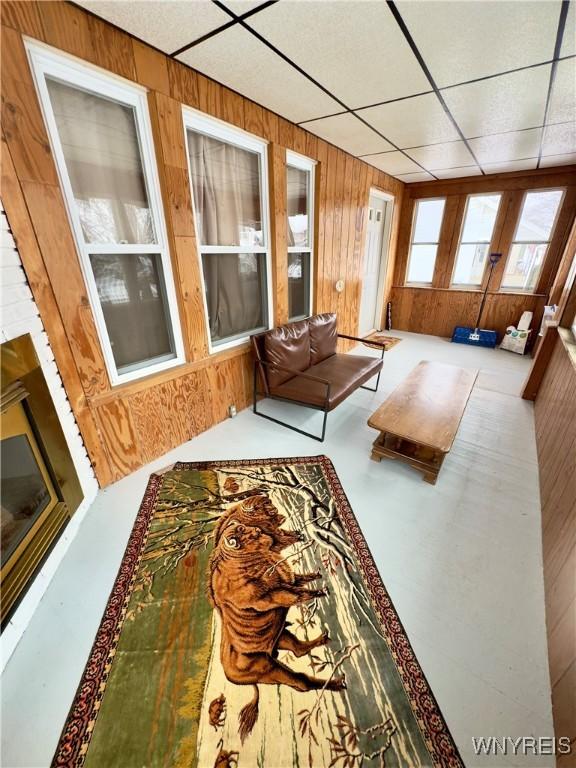 living area featuring wood walls, concrete floors, and a drop ceiling