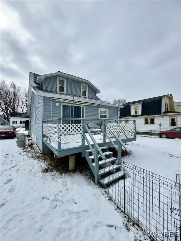 snow covered house with fence and a wooden deck