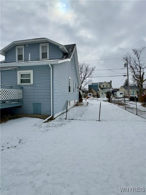 view of snow covered exterior with driveway and fence