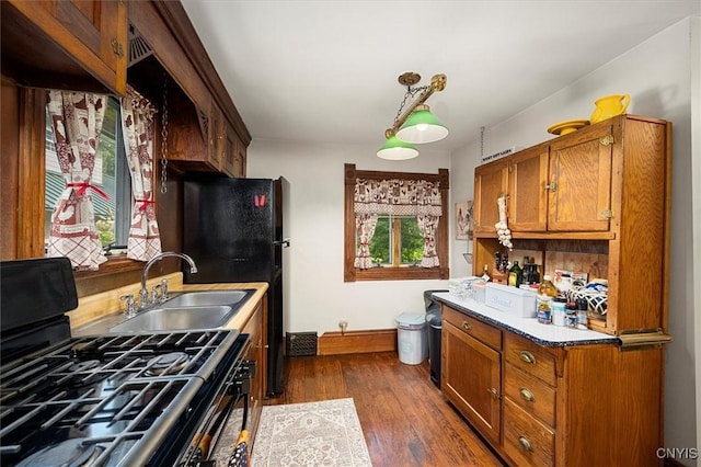 kitchen with dark wood-type flooring, a sink, brown cabinets, black appliances, and pendant lighting