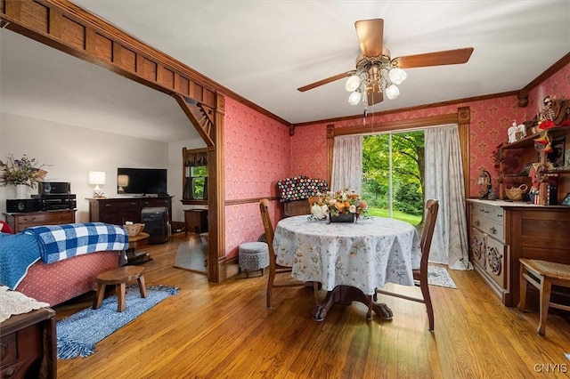 dining space with light wood-style floors, ornamental molding, and wallpapered walls