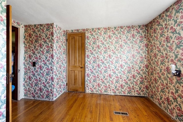 unfurnished room with wallpapered walls, visible vents, and wood finished floors