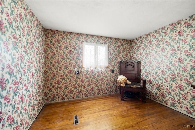 unfurnished room featuring wallpapered walls, visible vents, and wood finished floors