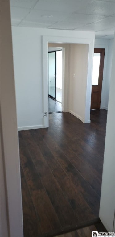 spare room with baseboards and dark wood-type flooring