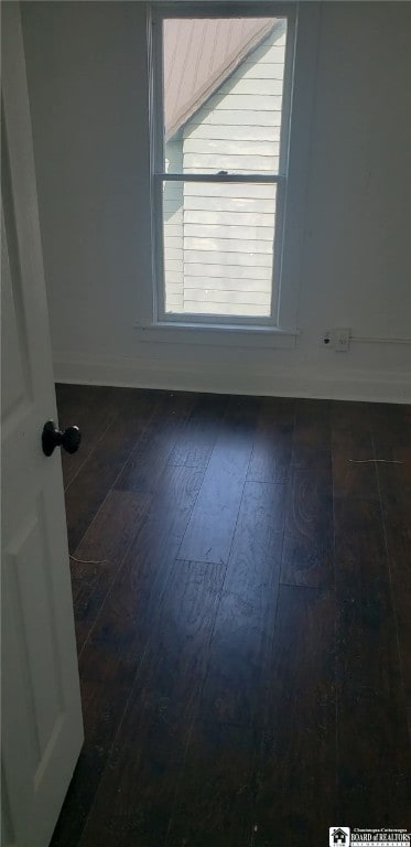 spare room with baseboards and dark wood-style flooring