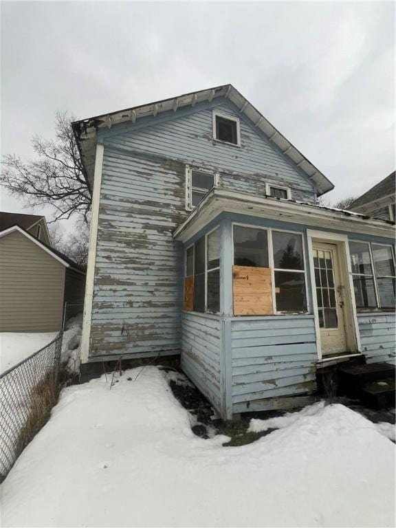 snow covered back of property featuring fence and a sunroom