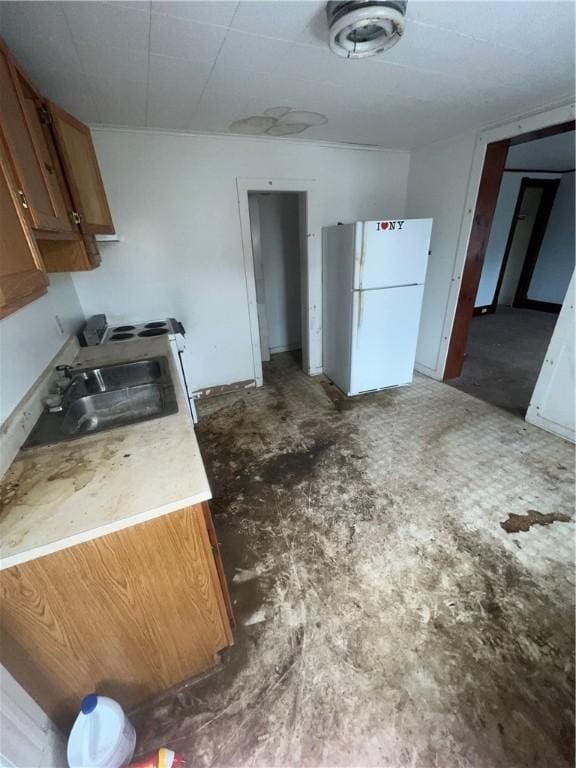 kitchen with freestanding refrigerator, brown cabinets, a sink, and unfinished concrete floors