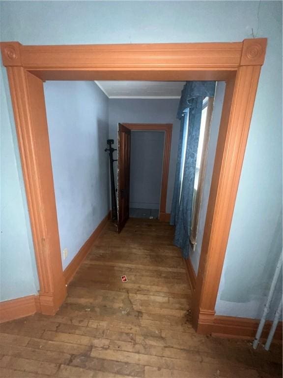 hallway featuring ornamental molding, wood-type flooring, and baseboards