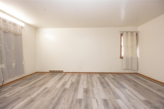 empty room featuring wood finished floors, visible vents, and baseboards