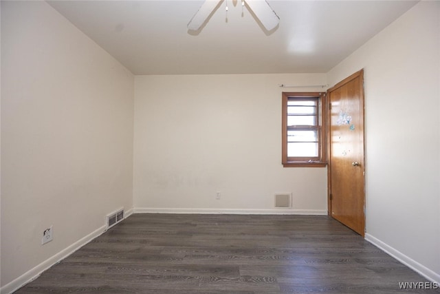 spare room with dark wood-type flooring, a ceiling fan, visible vents, and baseboards