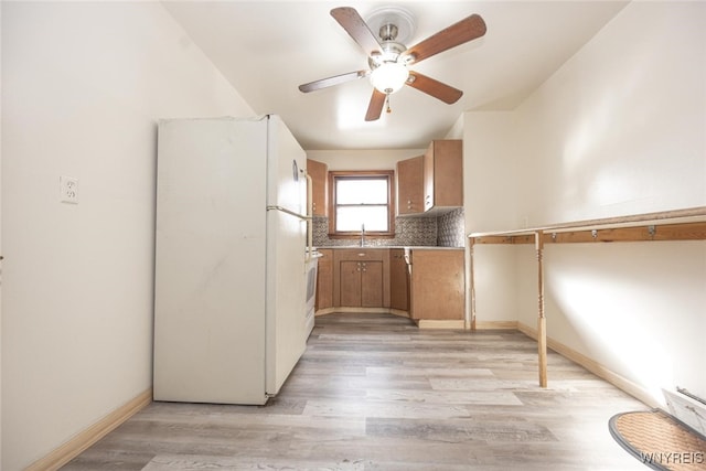 kitchen featuring a sink, baseboards, light wood-style floors, backsplash, and freestanding refrigerator