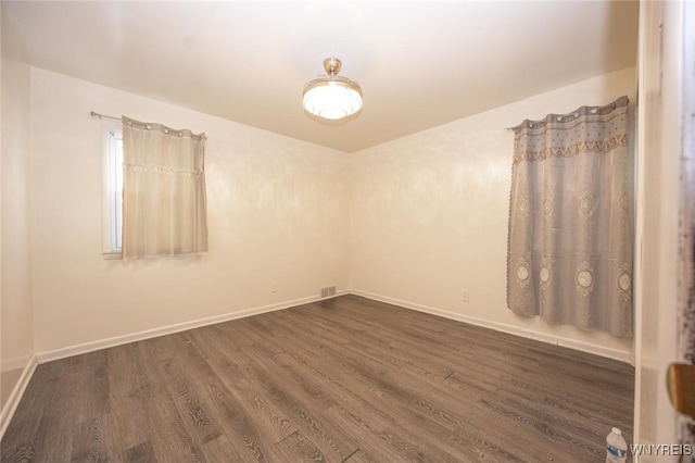 spare room with dark wood-style flooring, visible vents, and baseboards