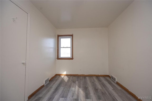 empty room featuring wood finished floors, visible vents, and baseboards