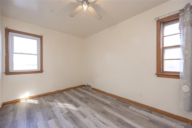 spare room featuring light wood finished floors, baseboards, visible vents, and a ceiling fan