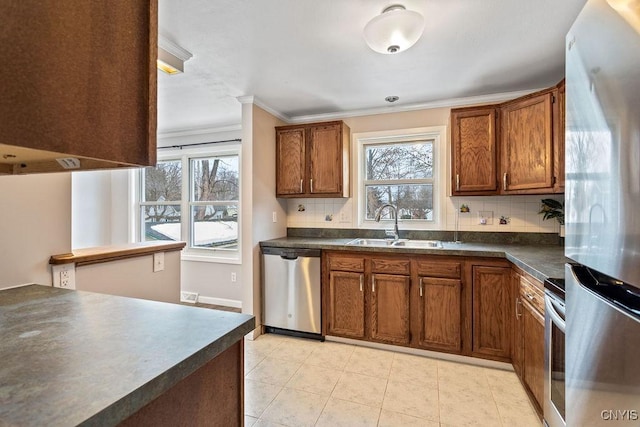 kitchen featuring crown molding, stainless steel appliances, dark countertops, brown cabinetry, and a sink