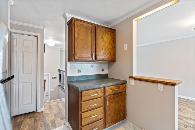 kitchen featuring dark countertops, decorative backsplash, brown cabinetry, ornamental molding, and wood finished floors