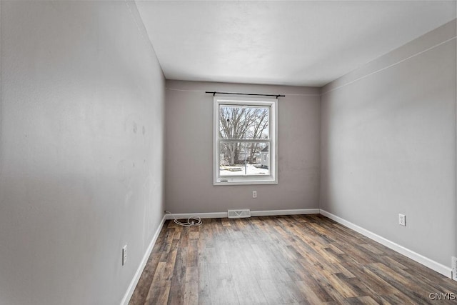 spare room with dark wood finished floors, visible vents, and baseboards