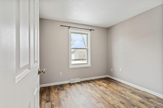 empty room with wood finished floors, visible vents, and baseboards