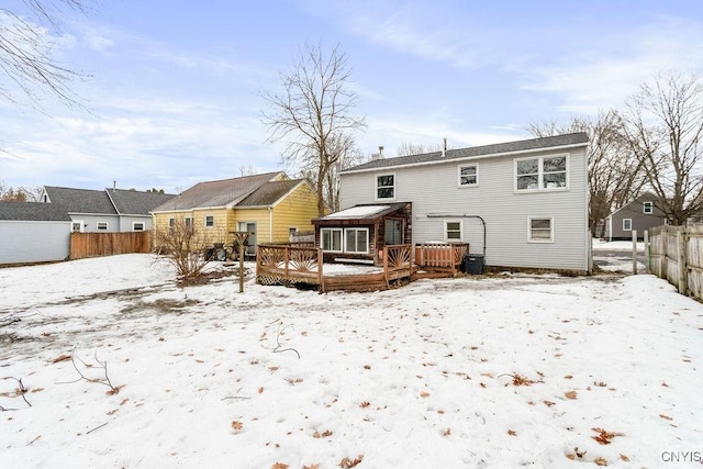 snow covered house featuring fence, a wooden deck, and central AC unit