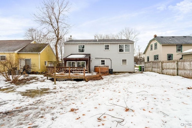 snow covered house featuring a chimney, fence, and a wooden deck